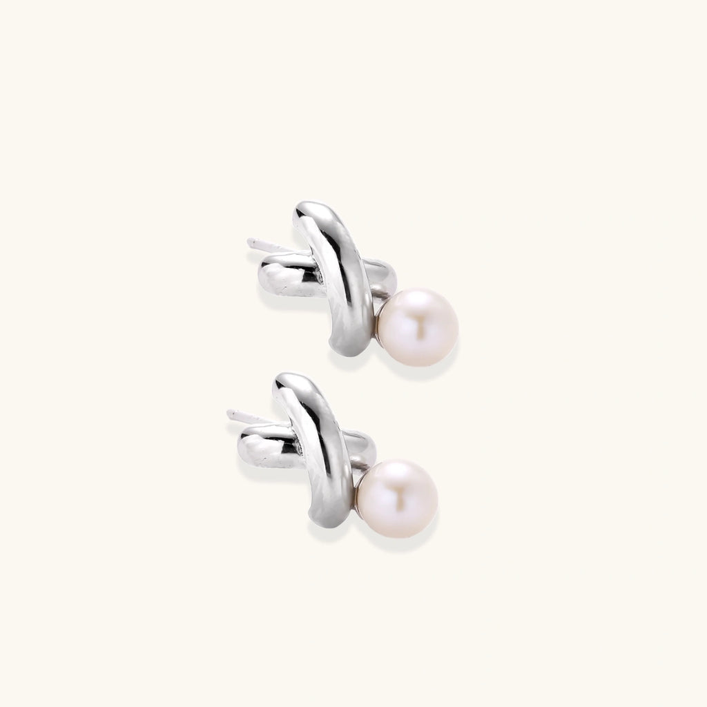Rhodium-plated silver earrings with twisted X design and freshwater pearl drops on beige background