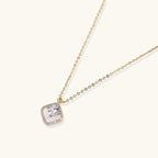 Gold quatrefoil pendant with crystal center on iridescent mother-of-pearl base, adjustable gold chain on cream background