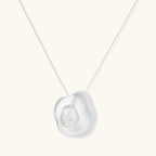 Sculptural silver necklace with flowing organic pendant featuring centered baroque pearl on white background.