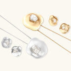 Sculptural silver necklace with flowing organic pendant featuring centered baroque pearl on white background.