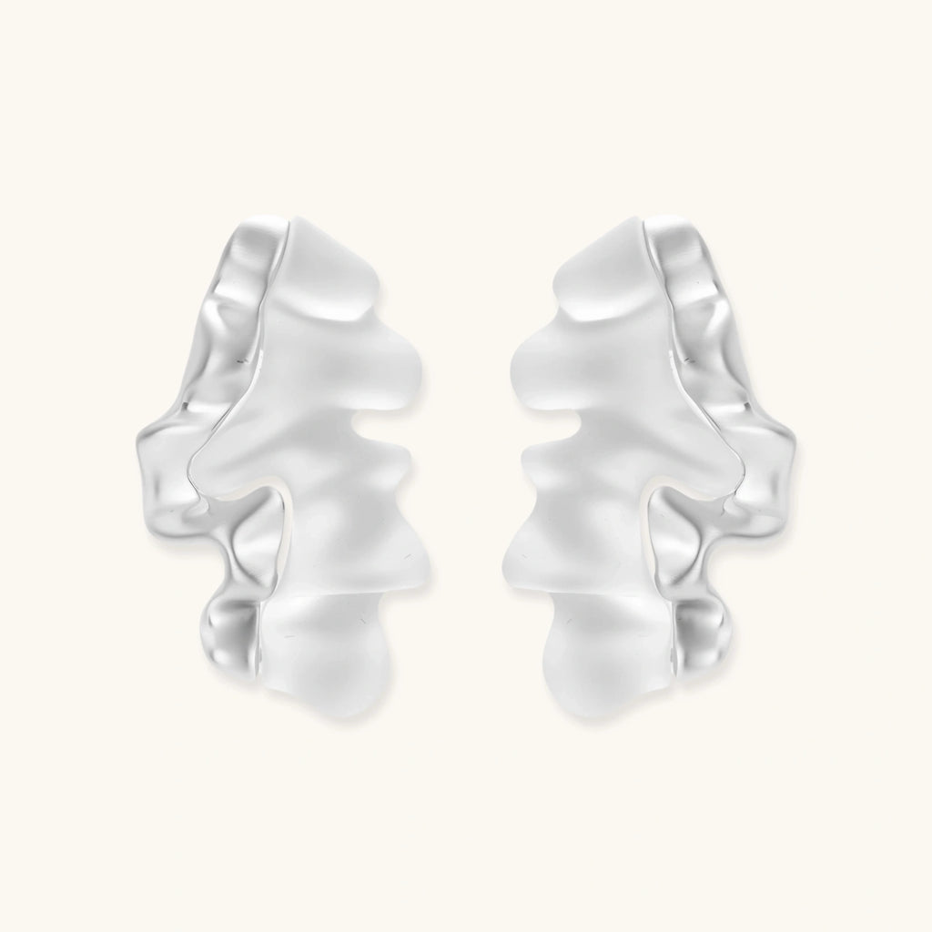 Pair of silver-toned sculptural earrings with flowing abstract forms and stud backs against white background.