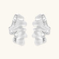 Pair of silver-toned sculptural earrings with flowing abstract forms and stud backs against white background.