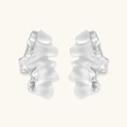 Pair of silver-toned sculptural earrings with flowing abstract forms and stud backs against white background.