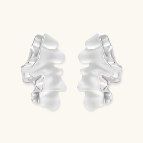 Pair of silver-toned sculptural earrings with flowing abstract forms and stud backs against white background.