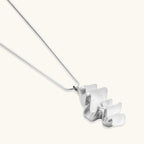Modern sculptural pendant necklace with twisted metallic design on delicate silver chain against neutral background.