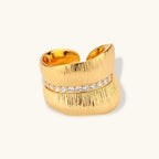 Adjustable gold-plated cuff ring with parallel ridged texture and diagonal row of sparkling zirconia stones on white background.